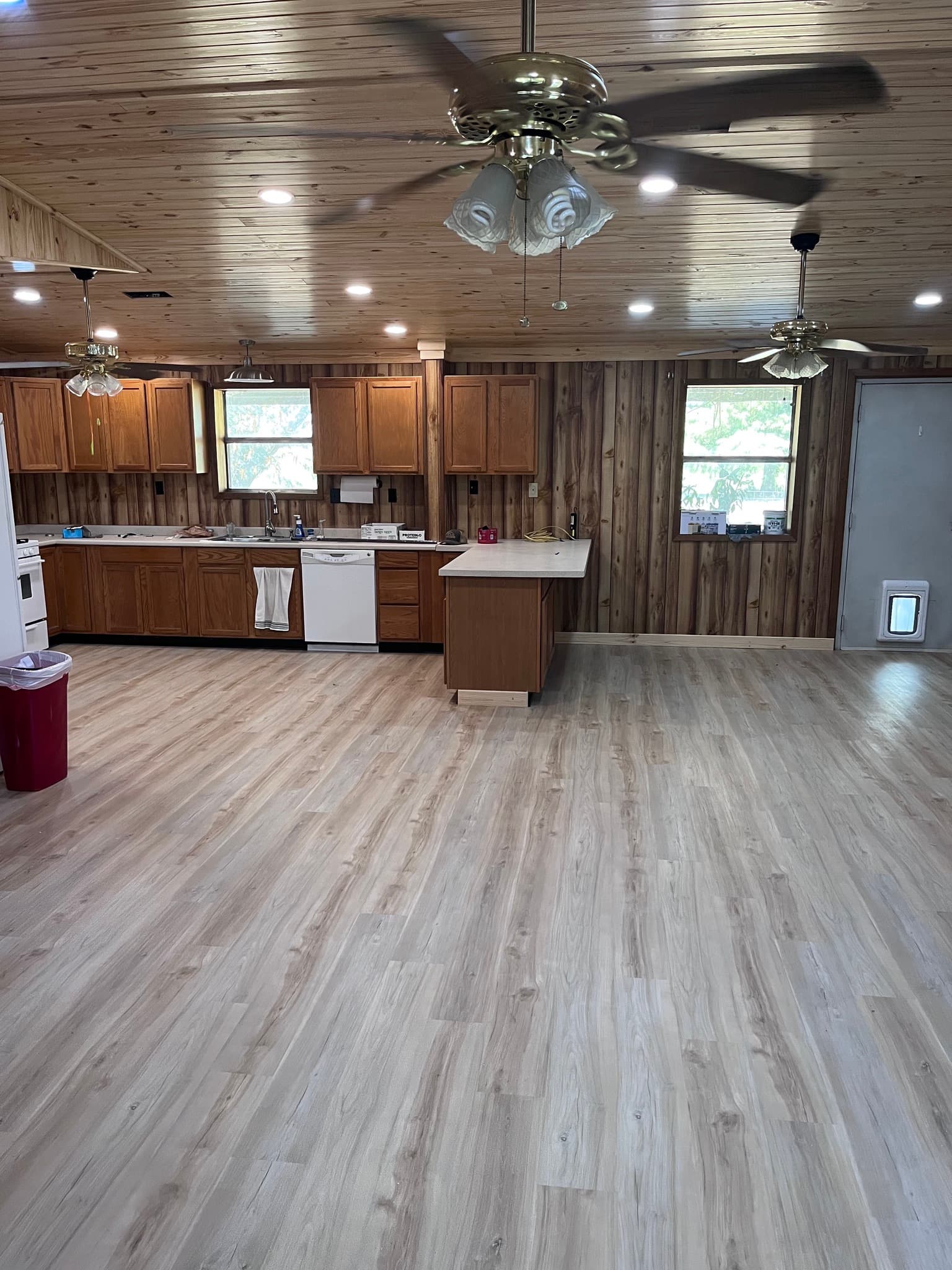 Spacious kitchen with wood-paneled walls and ceiling, light wood floors, and multiple ceiling fans.