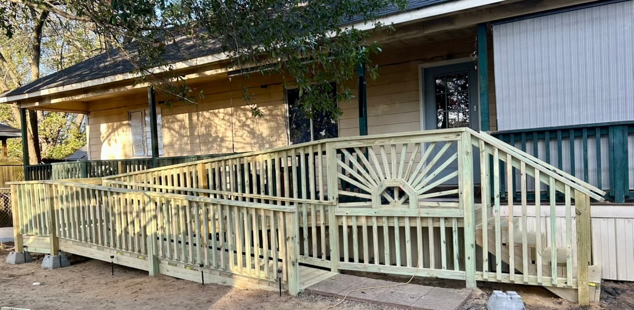 Wooden accessibility ramp with a decorative sunburst railing leading to a house's front porch.