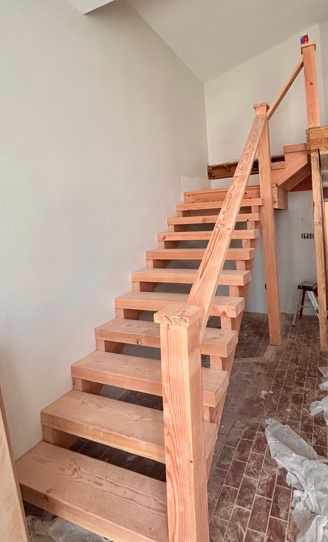 Unfinished light wood staircase with open risers and a handrail in a construction site.
